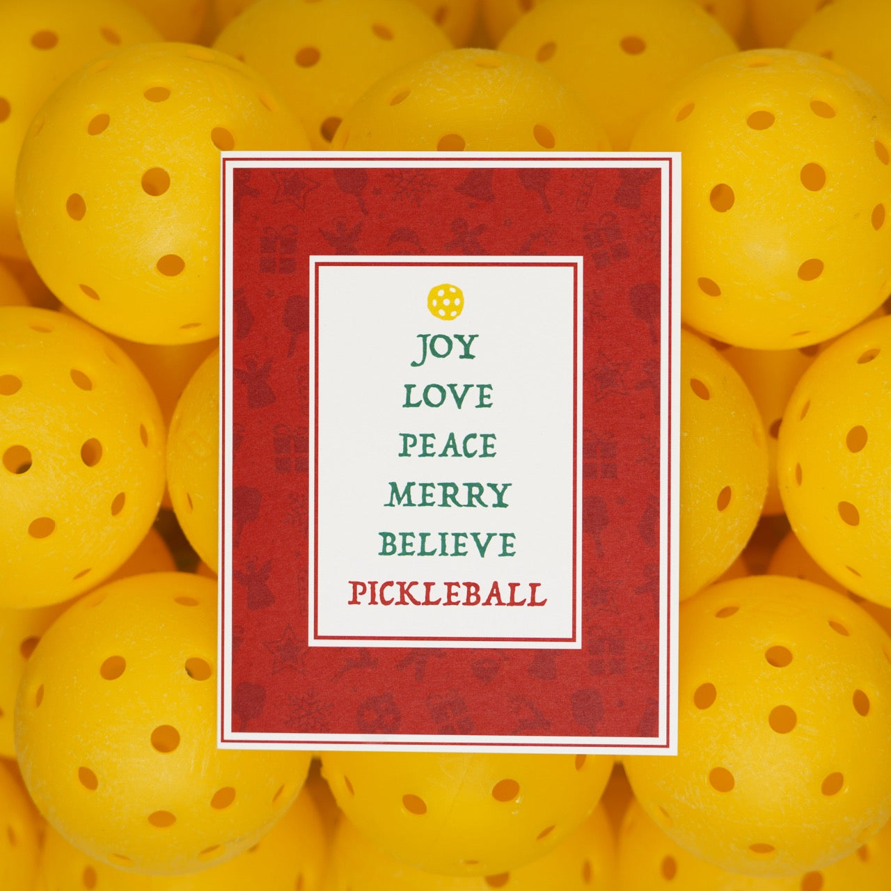 Pickleball themed Christmas card sitting on top of a pile of pickleballs.