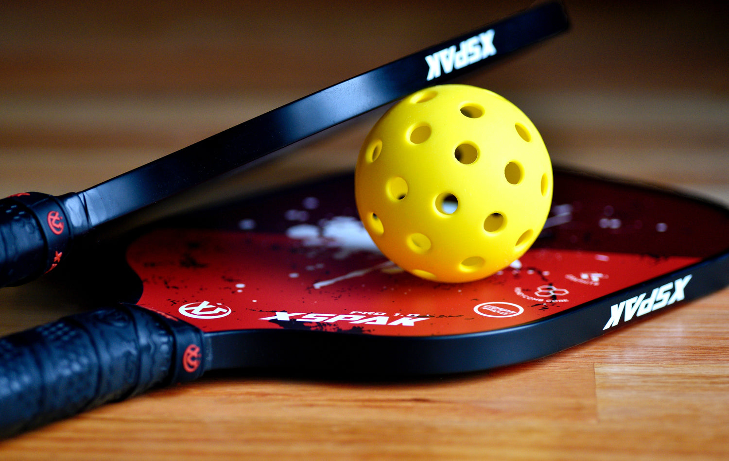 Two black and red pickleball paddles and a pickleball ball