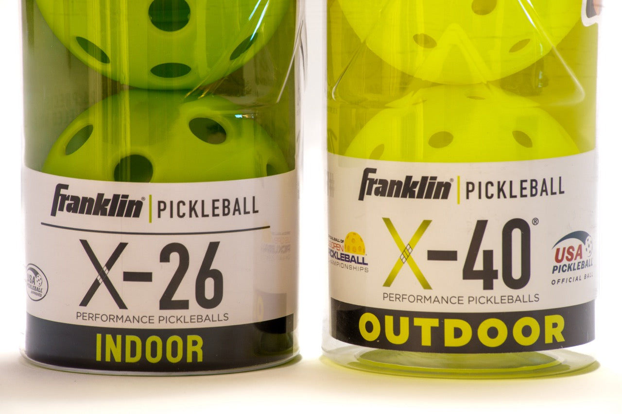 Can of indoor pickleballs next to a can of outdoor pickleballs