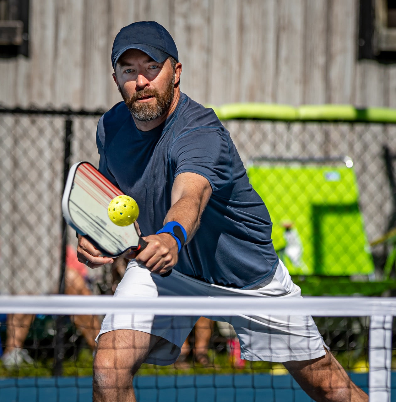 A man stretching to hit a pickleball over the net in front of him