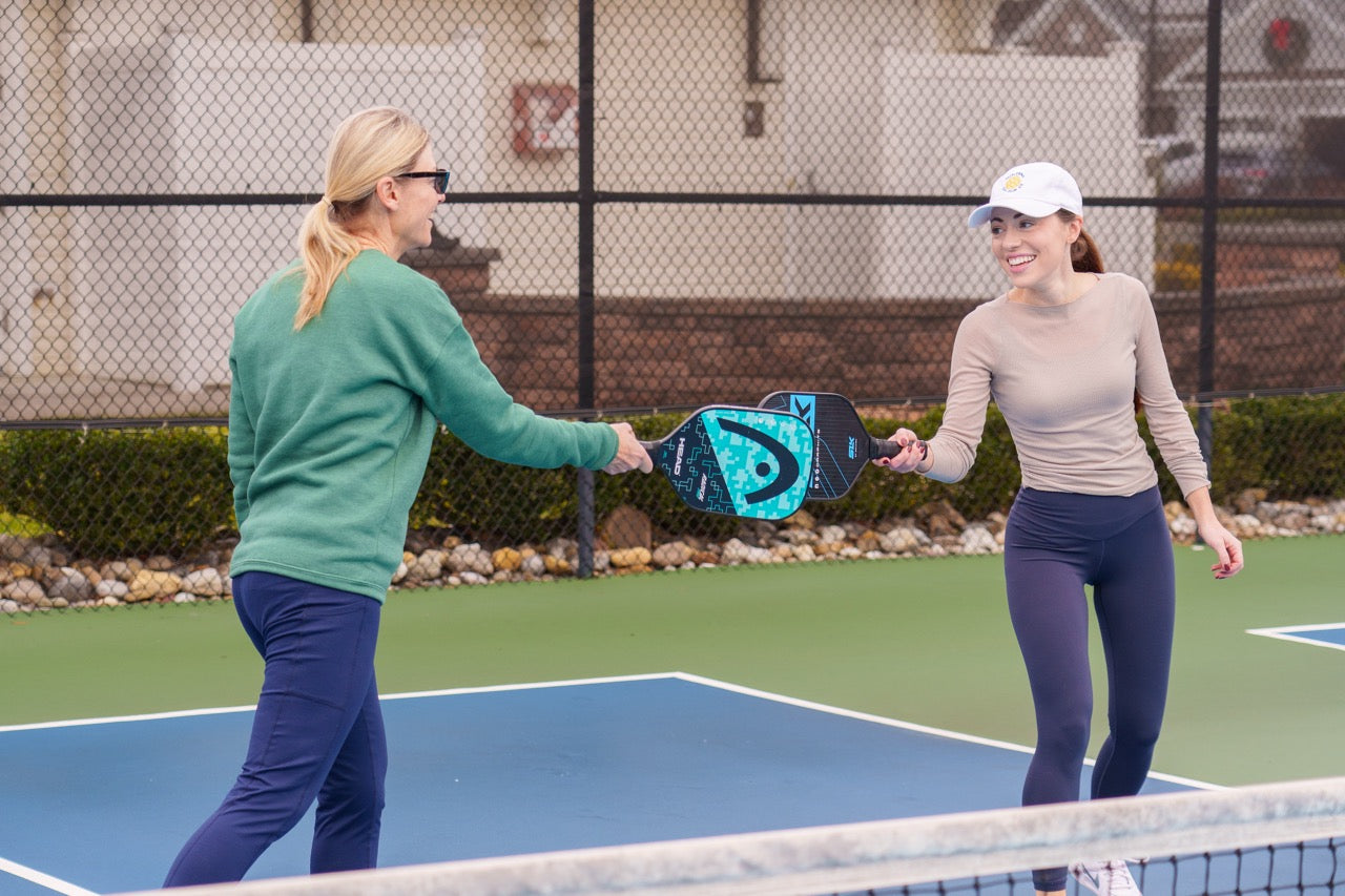 Two women tapping their pickleball paddles together