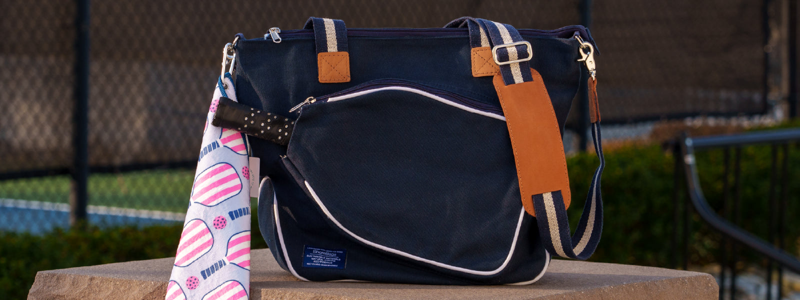 Navy blue canvas pickleball bag sitting on a ledge with a pickleball themed towel hanging off.