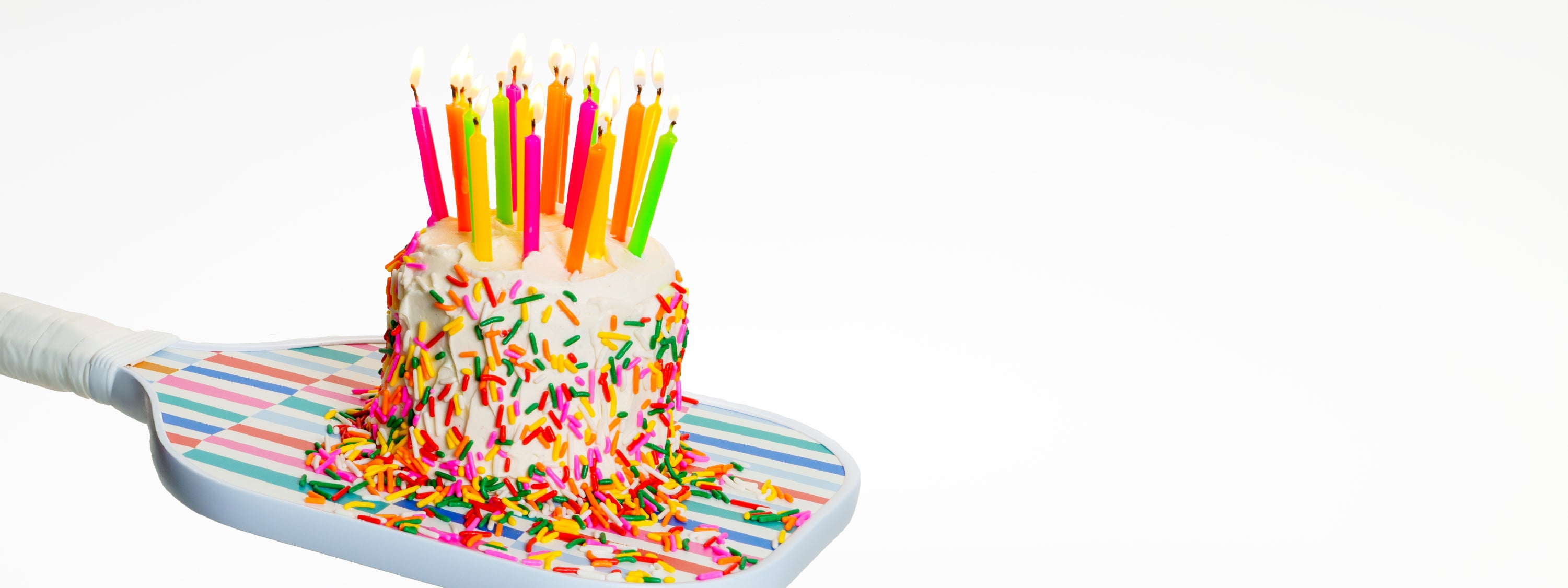 Birthday cake sitting on top of a pickleball paddle with candles that are lit.