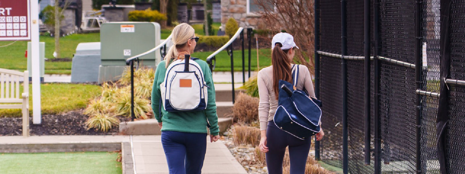 Two women walking to pickleball courts with stylish pickleball apparel and bags.