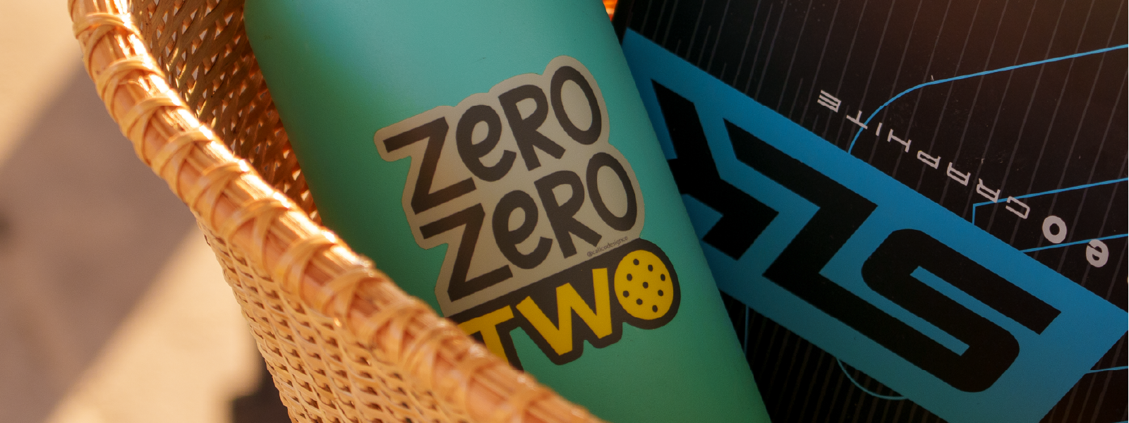 Close up of a water bottle and pickleball paddle with a vinyl sticker on the bottle that says ZERO ZERO TWO