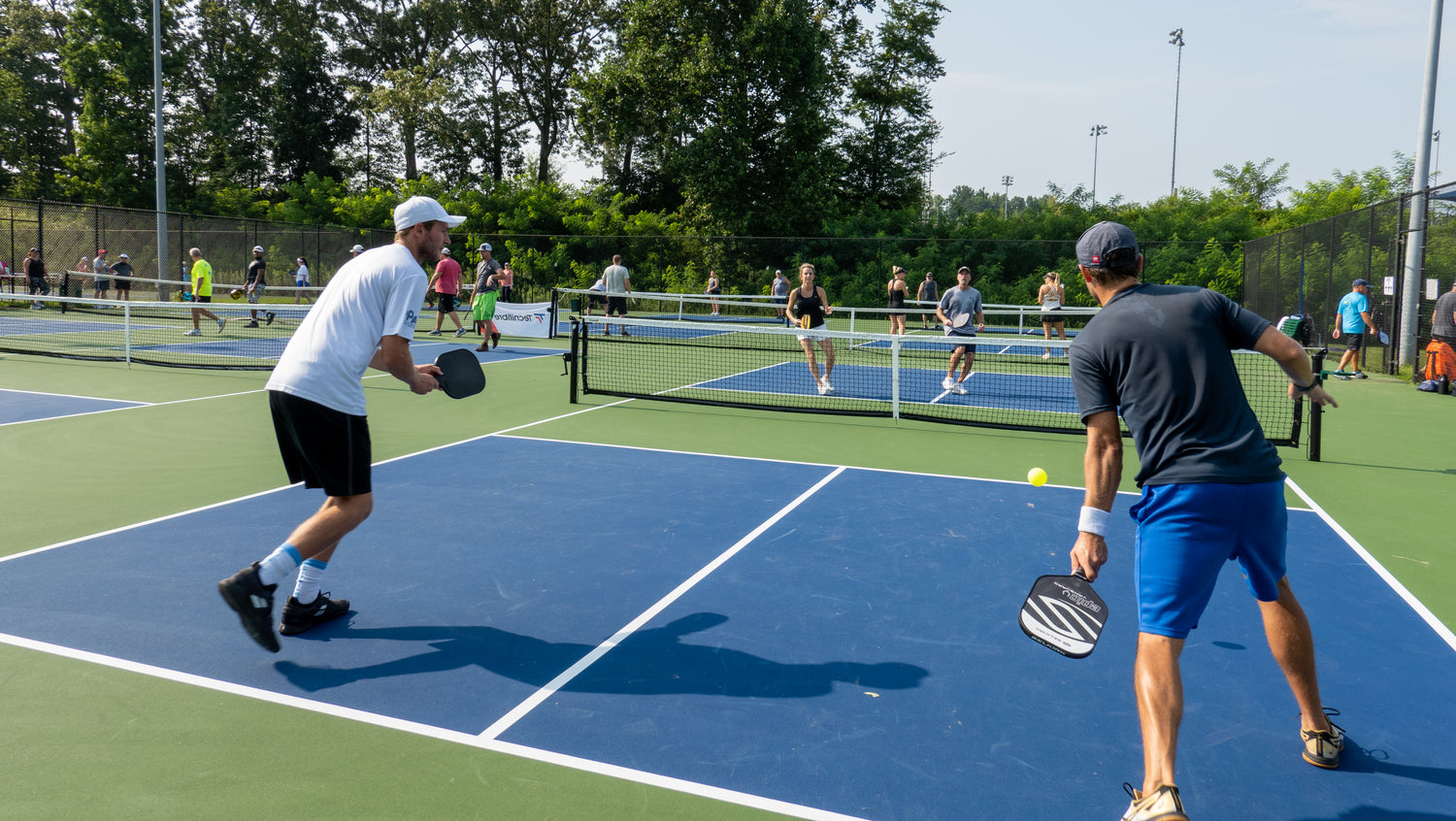 Two men playing pickleball with the man on the right about to perform a 3rd shot drop