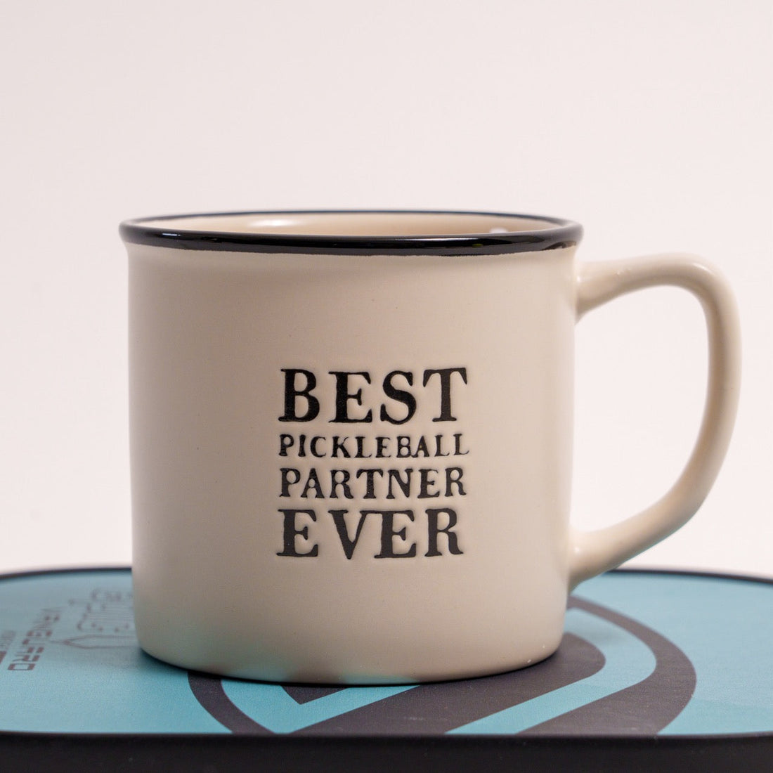 Stoneware coffee mug that says Best Pickleball Partner Ever on it sitting on a pickleball paddle