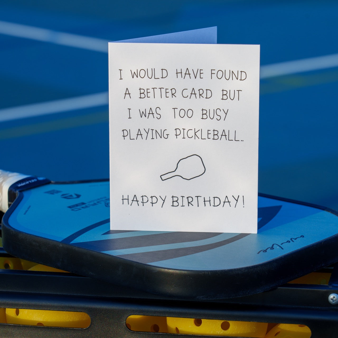 Funny pickleball birthday card that says &quot;I would have found a better card but I was too busy playing pickleball... Happy Birthday&quot; with a crudely drawn pickleball paddle standing up on a pickleball paddle with balls