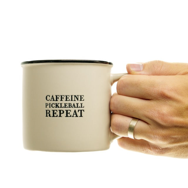 Stoneware coffee mug that says Caffeine Pickleball Repeat on it being held by a man.