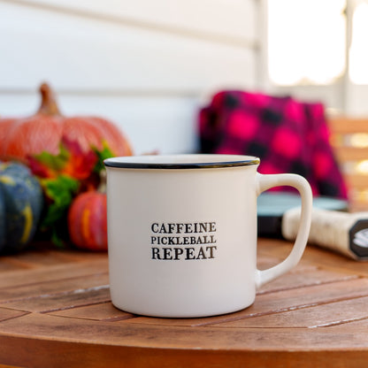 Stoneware coffee mug that says Caffeine Pickleball Repeat on a table in front of pumpkins and a blanket