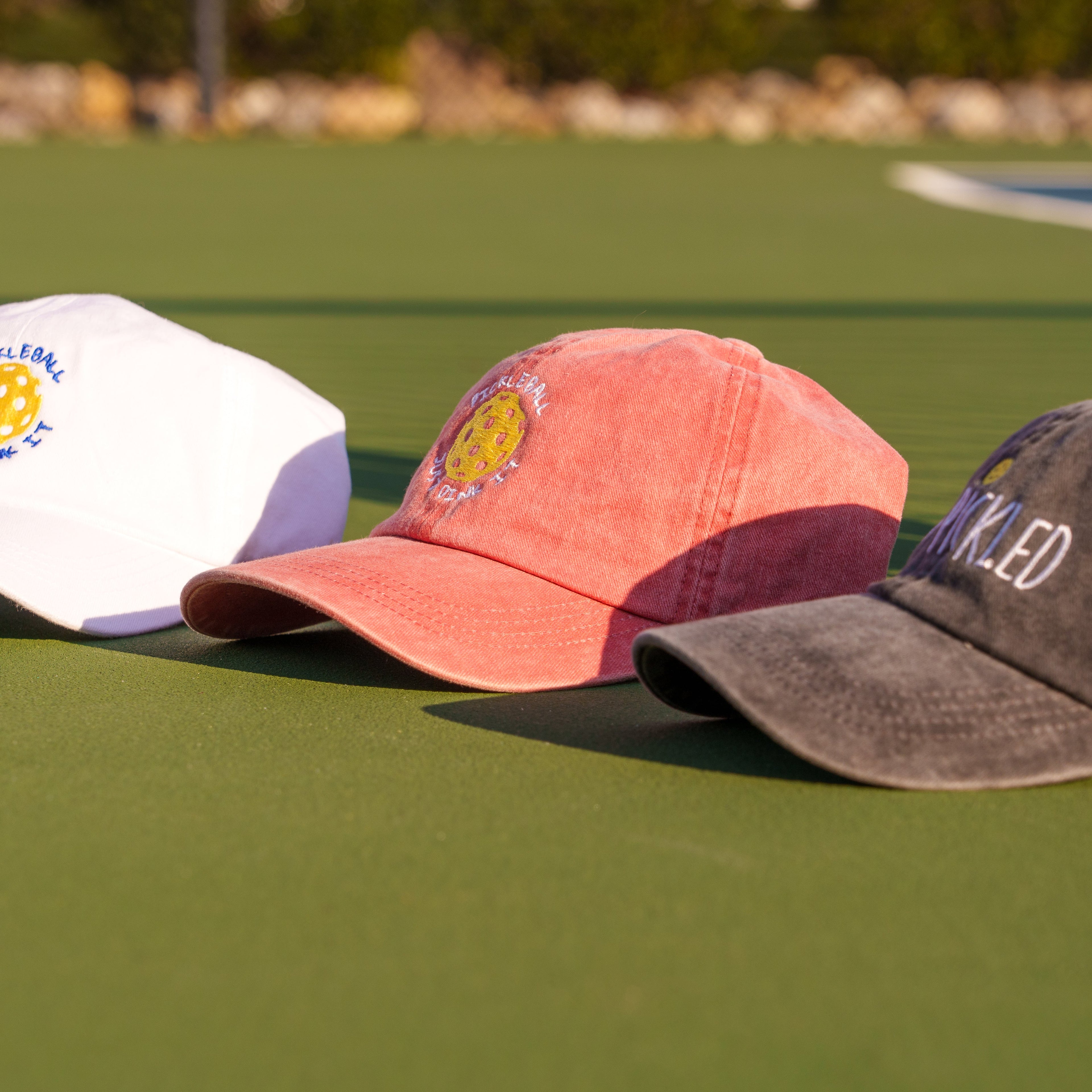 Collection of three different color pickleball baseball hats sitting on a pickleball court