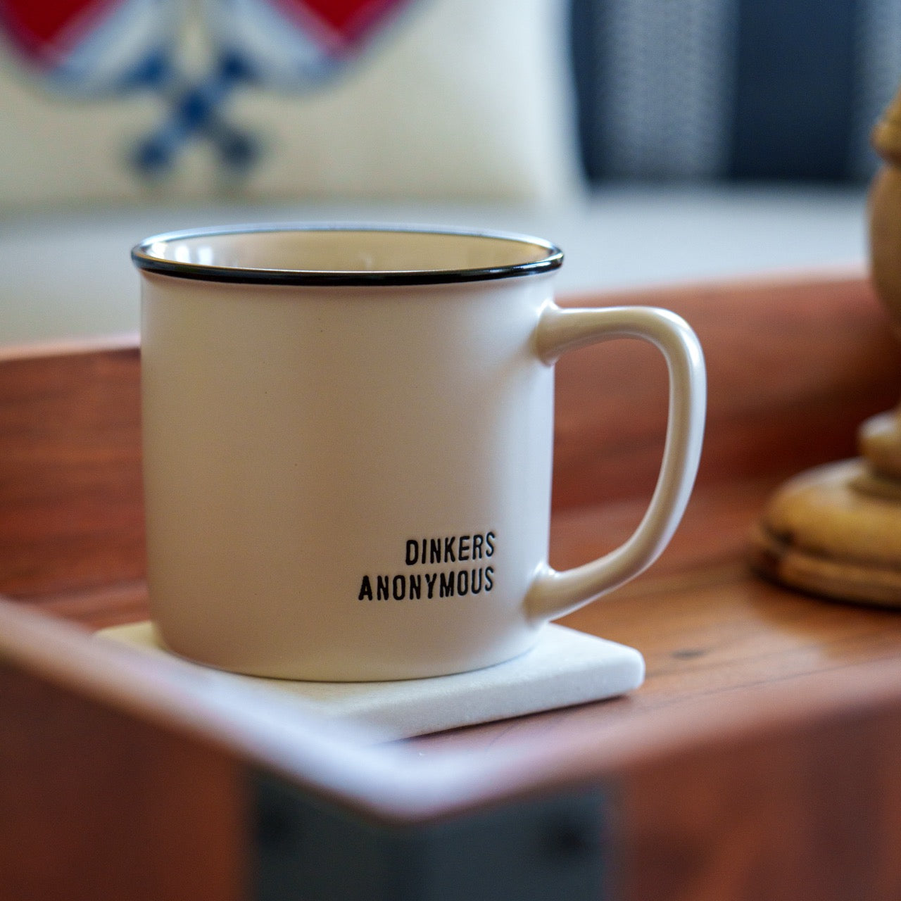 Humorous stoneware coffee mug that says Dinkers Anonymous on it sitting on a coffee table.