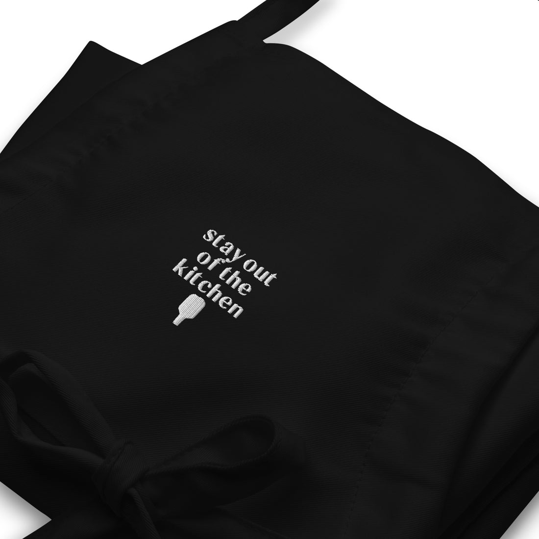 Detailed view of folded embroidered black apron that says &quot;stay out of the kitchen&quot; and has a pickleball paddle on it