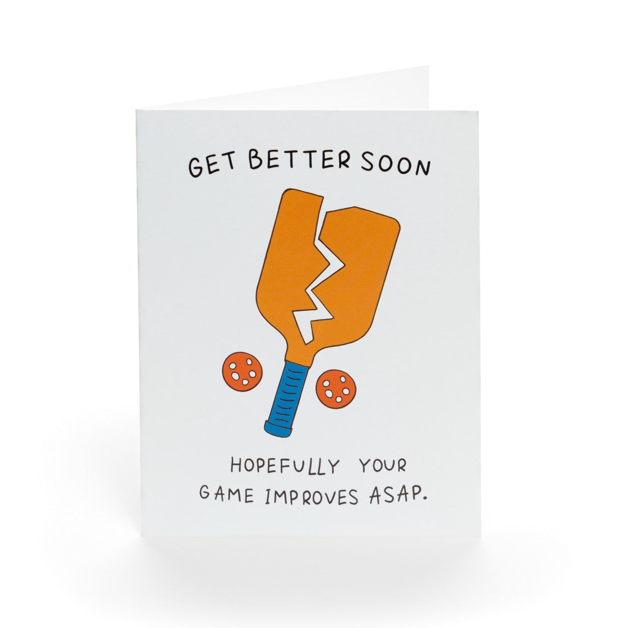 A funny pickleball themed get well soon greeting card that shows a broken paddle and two pickleballs with text that reads &quot;Get Better Soon, Hopefully your game improves ASAP.&quot; standing up in front of a white background