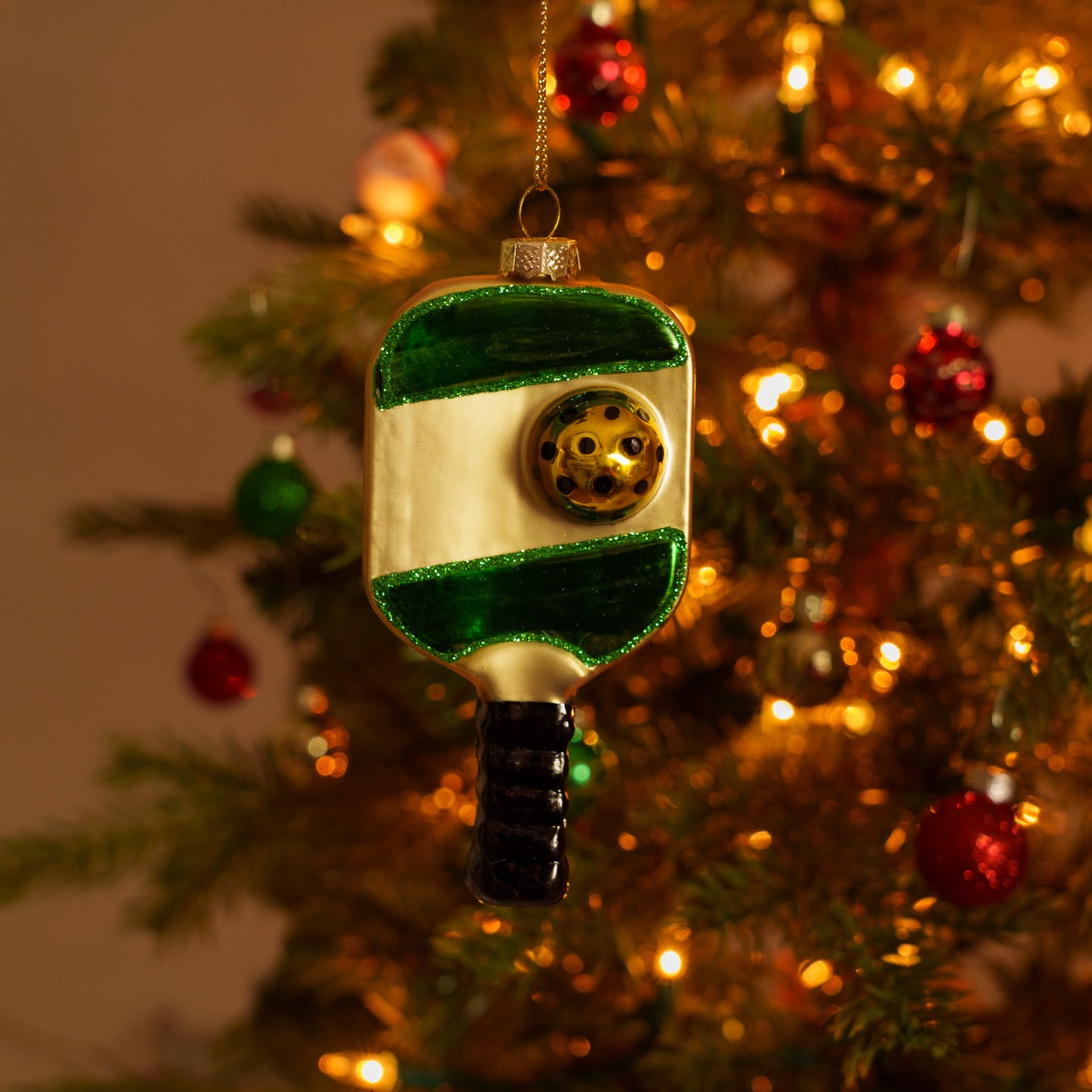 Handmade glass green and gold pickleball paddle Christmas ornament hanging on a Christmas tree