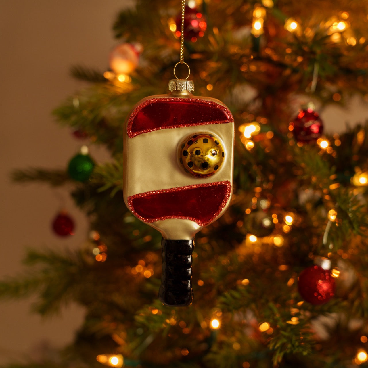 Handmade glass red and gold pickleball paddle Christmas ornament hanging on a Christmas tree with a pickleball