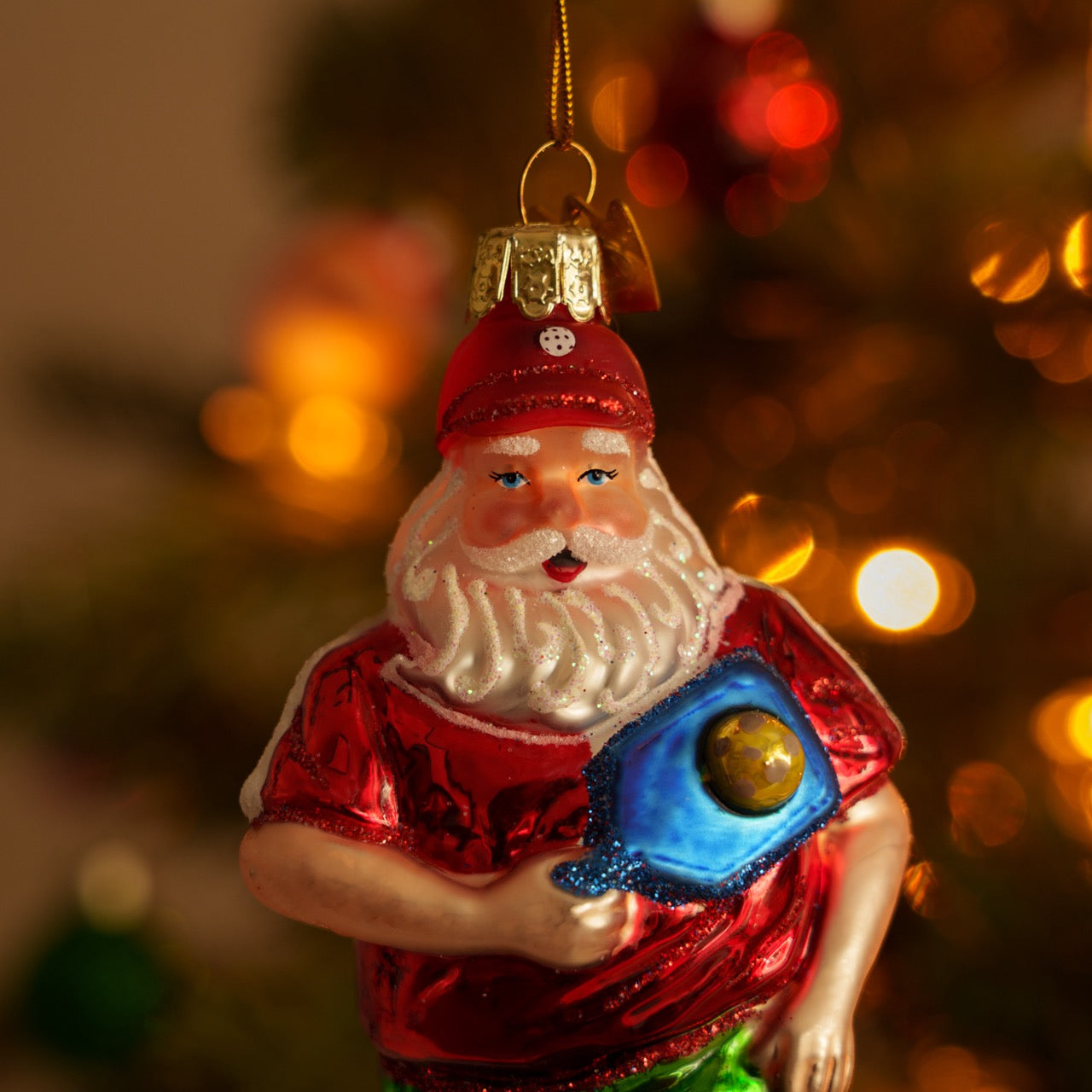 Close up of an elegant handmade glass Christmas ornament of Santa playing pickleball  hanging on a Christmas tree