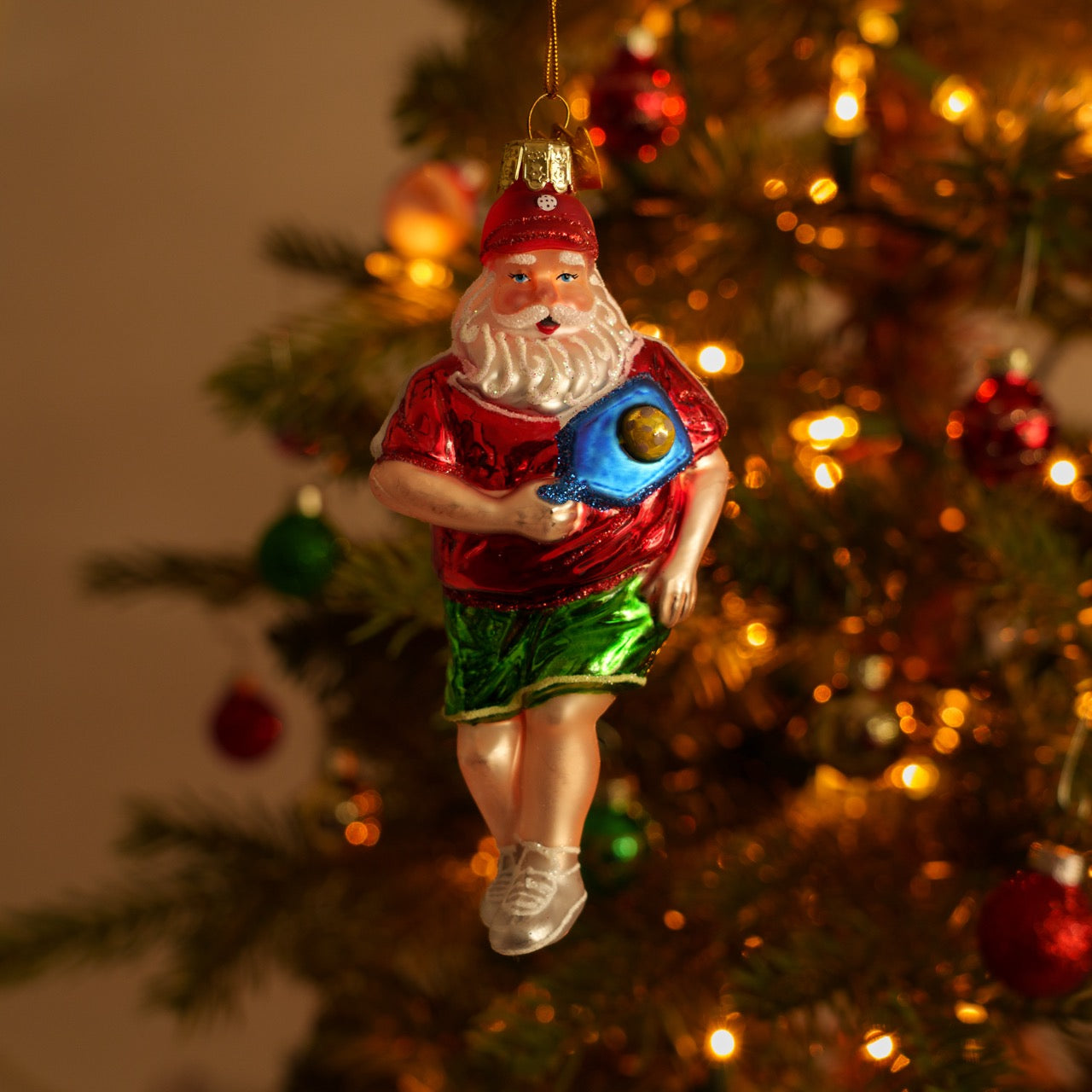 Elegant handmade glass Christmas ornament of Santa playing pickleball  hanging on a Christmas tree