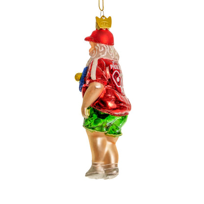 Left side of an elegant handmade glass Christmas ornament of Santa playing pickleball  hanging in front of a white studio backdrop