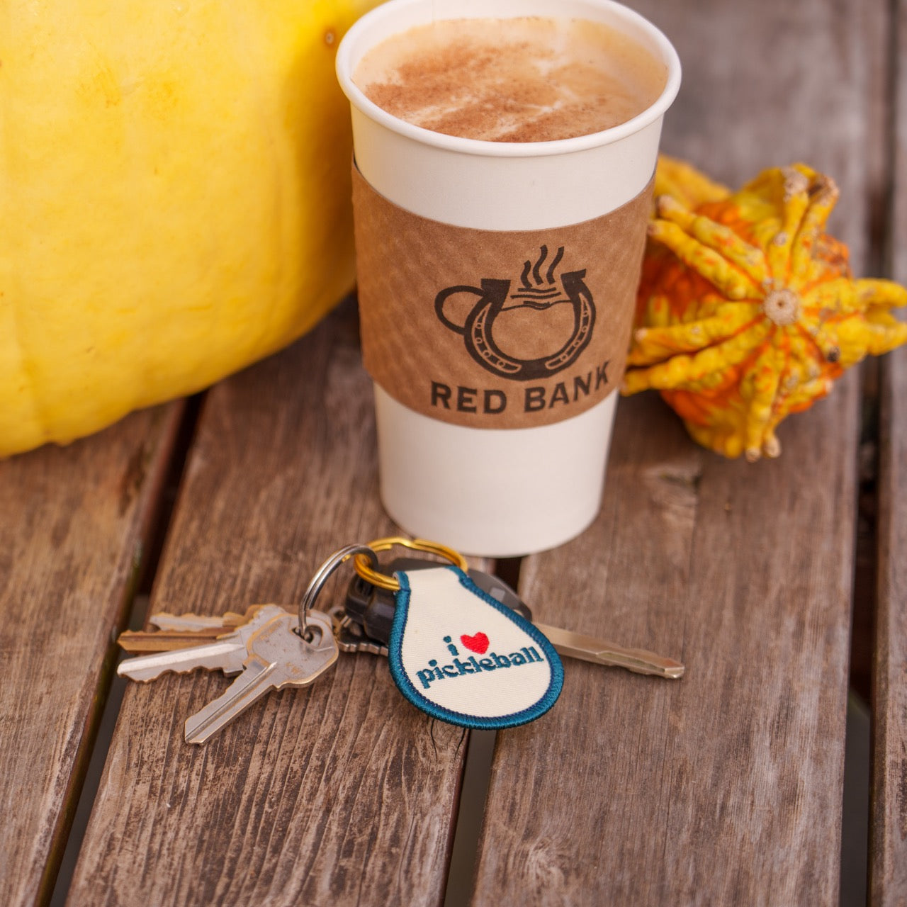 Keychain that says &quot;I heart pickleball&quot; on a table with keys, coffee and decorative fall gourds