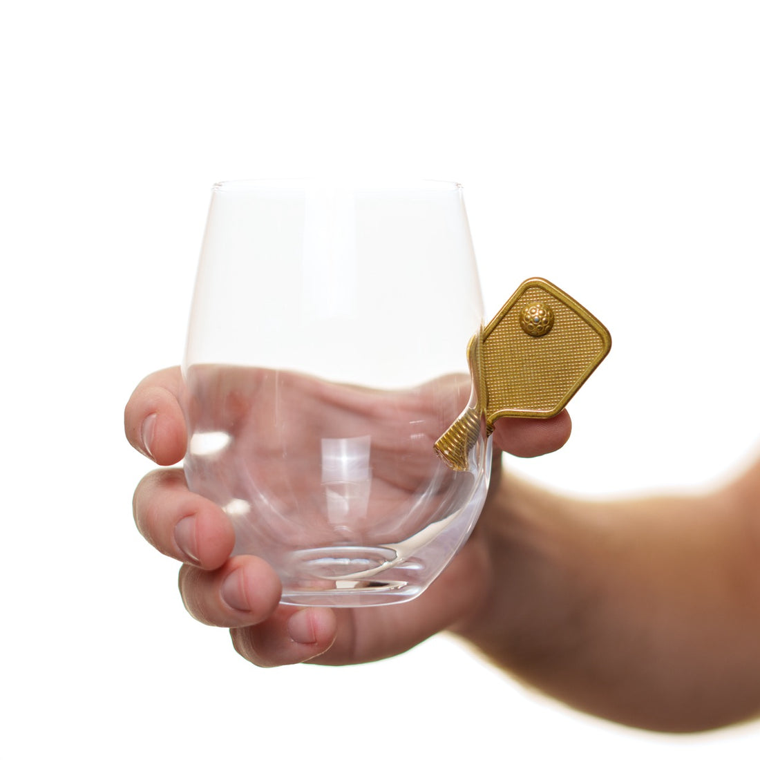 Person holding a unique wine glass with a small metal pickleball paddle protruding from the side in front of a white studio backdrop