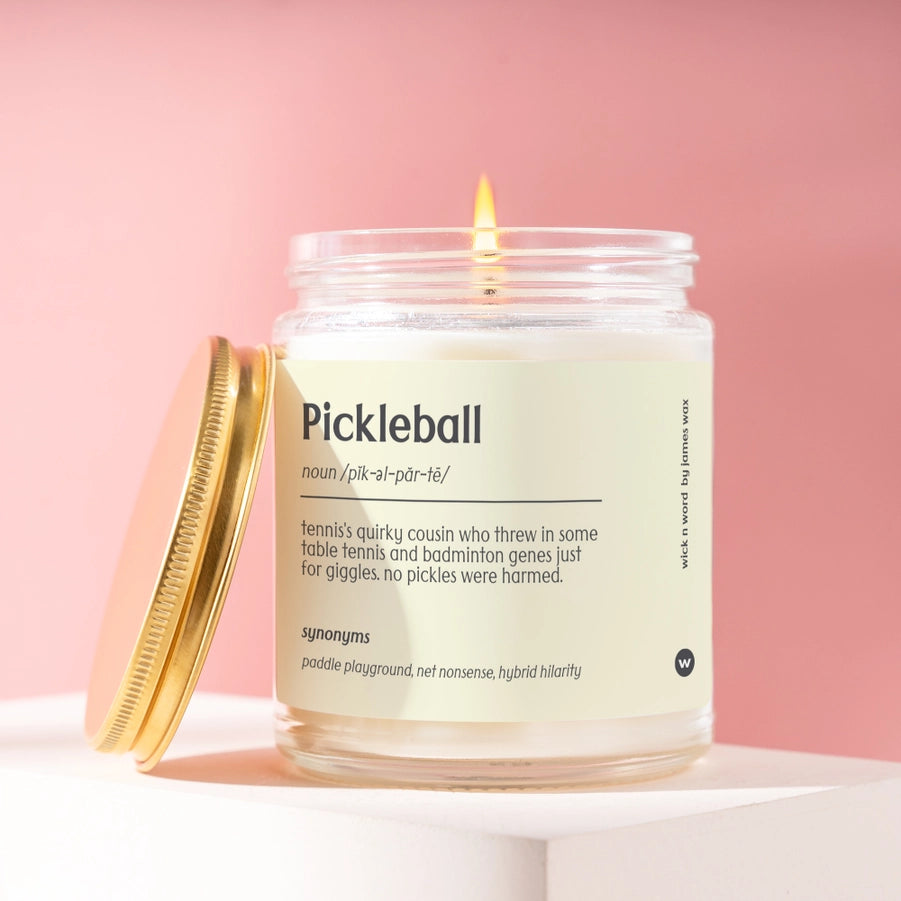 Lit pickleball definition candle with a cream label and pink background