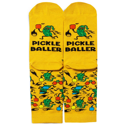 Soles of humorous yellow socks with pickles playing pickleball and say PICKLEBALLER on them