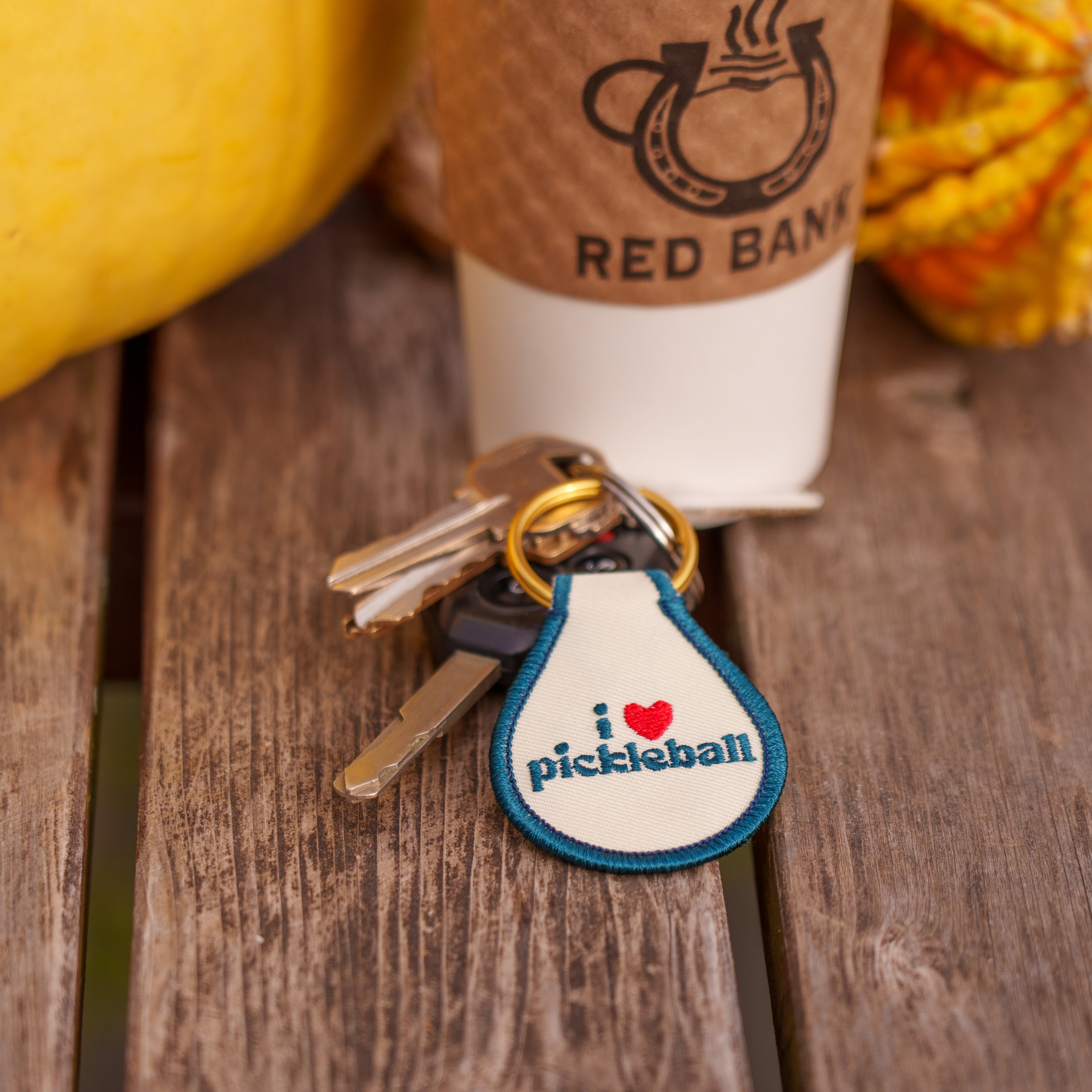 Close up coffee, two gourds, and keys with a key tag that says "I Love Pickleball" on a picnic table