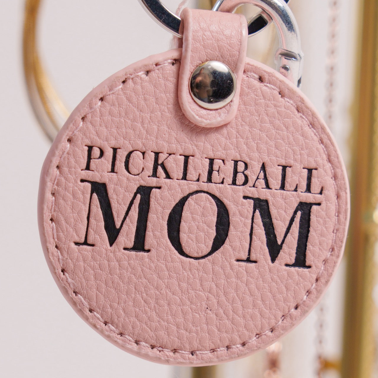 Pink keychain that says Pickleball Mom on it hanging on jewelry holder up close