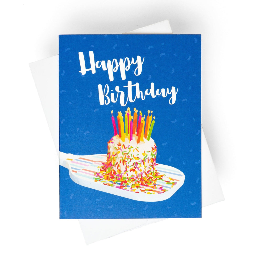 Colorful pickleball themed birthday card with a birthday cake with candles sitting on a pickleball paddle and big bold text that reads Happy Birthday laying flat on a white background.