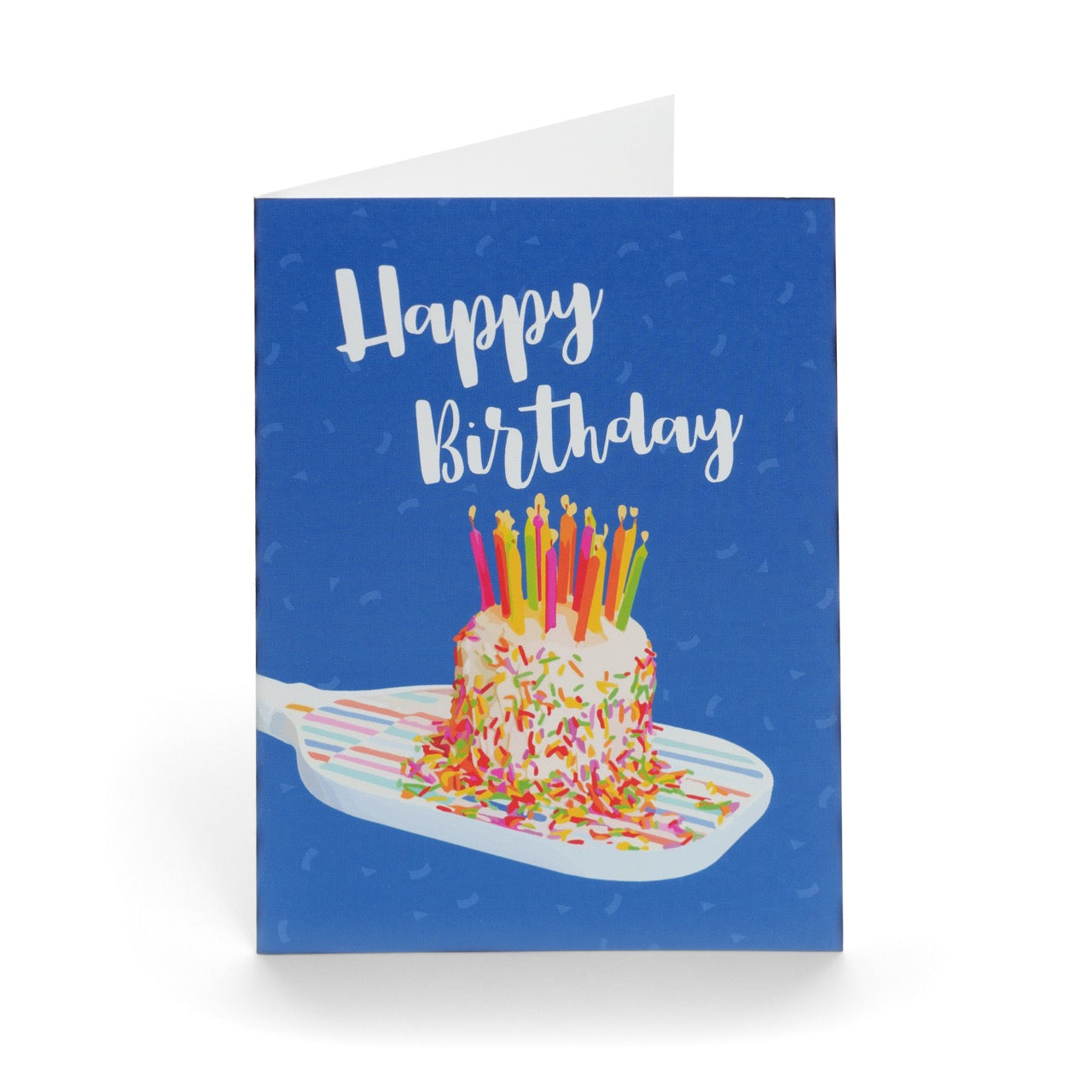 A fun colorful pickleball themed birthday card with a birthday cake with candles sitting on a pickleball paddle and big bold text that reads Happy Birthday standing up on a white background