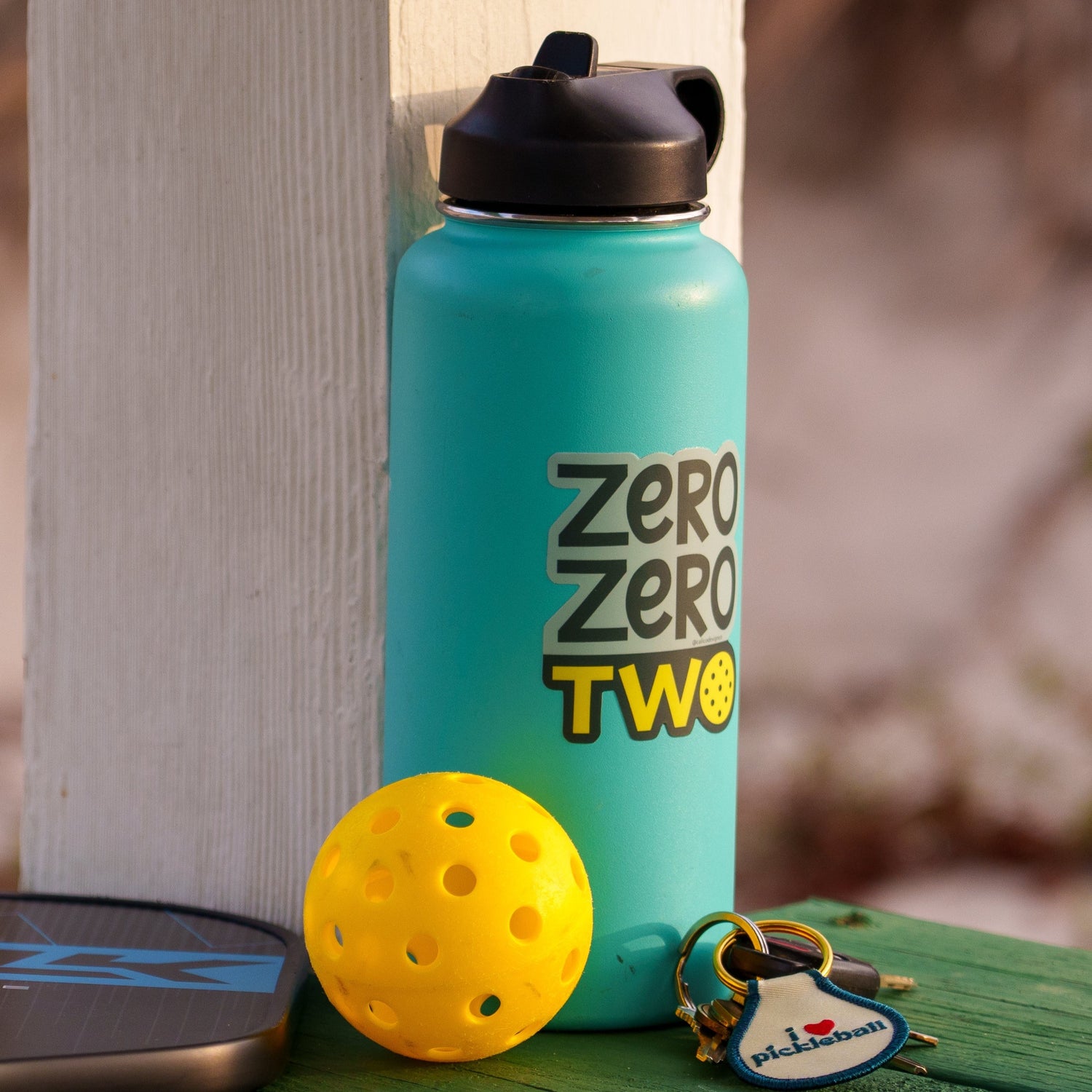 Blue water bottle with a pickleball-themed sticker on it that says &quot;ZERO ZERO TWO&quot; next to a pickleball paddle and ball