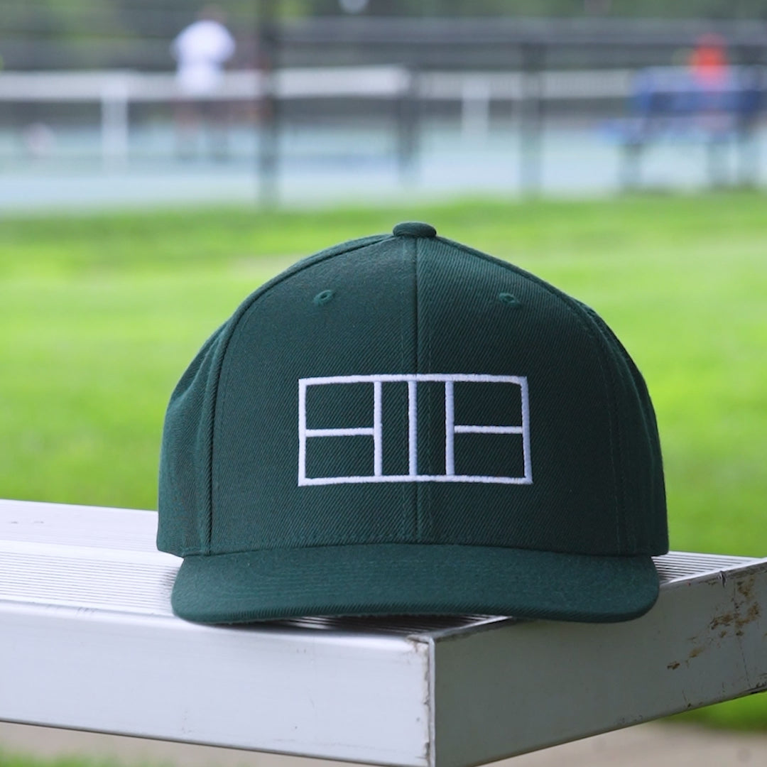 Video of a dark green snapback hat with a white embroidered pickleball court on it