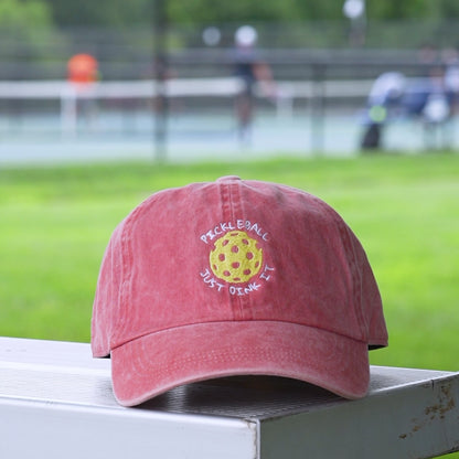 Video of a red baseball hat with a yellow embroidered pickleball and white words saying PICKLEBALL JUST DINK IT on it.