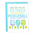 Pickleball-themed retirement card with pickleball paddles and balls on it laying flat