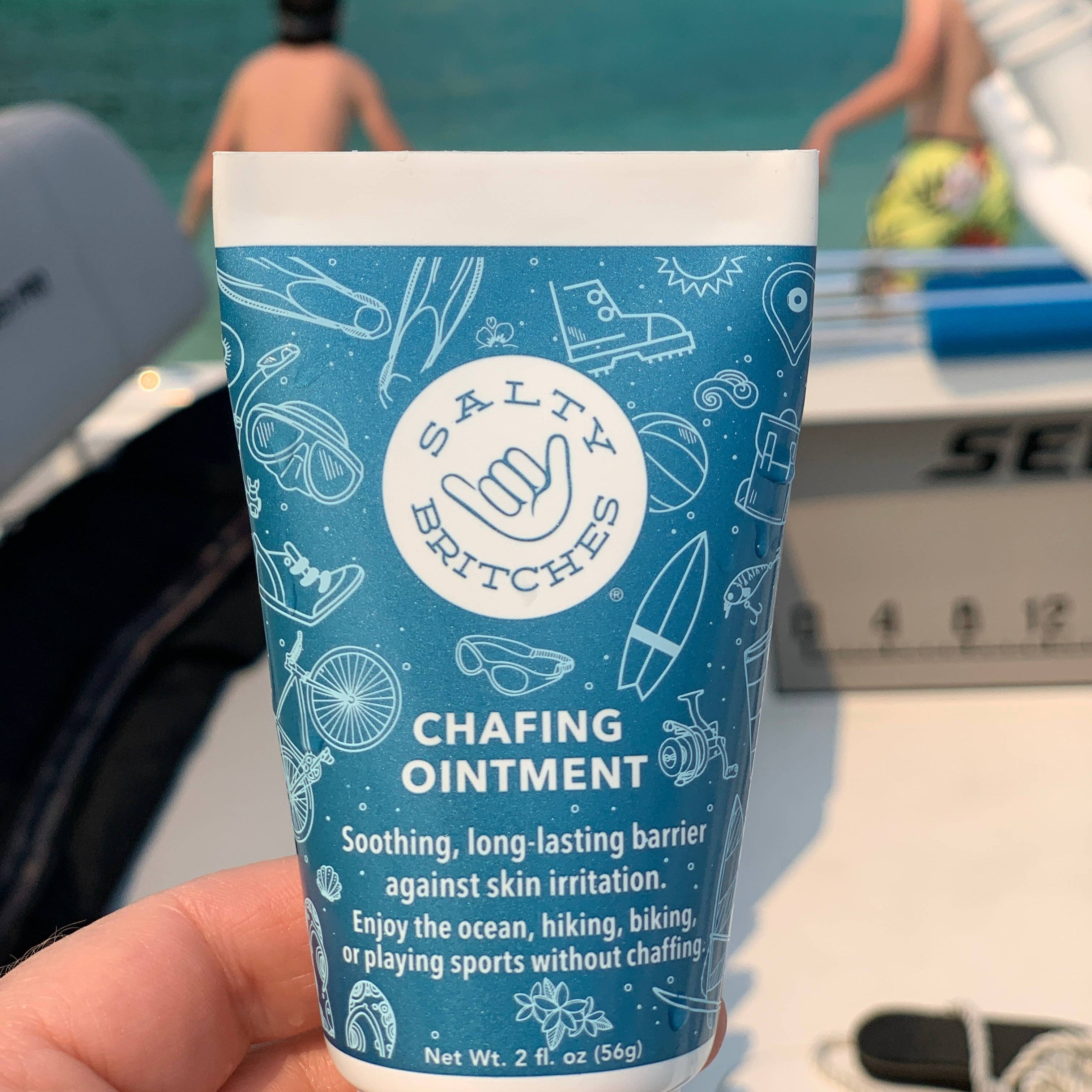 Person holding tube of chafing ointment with boat and water in the background