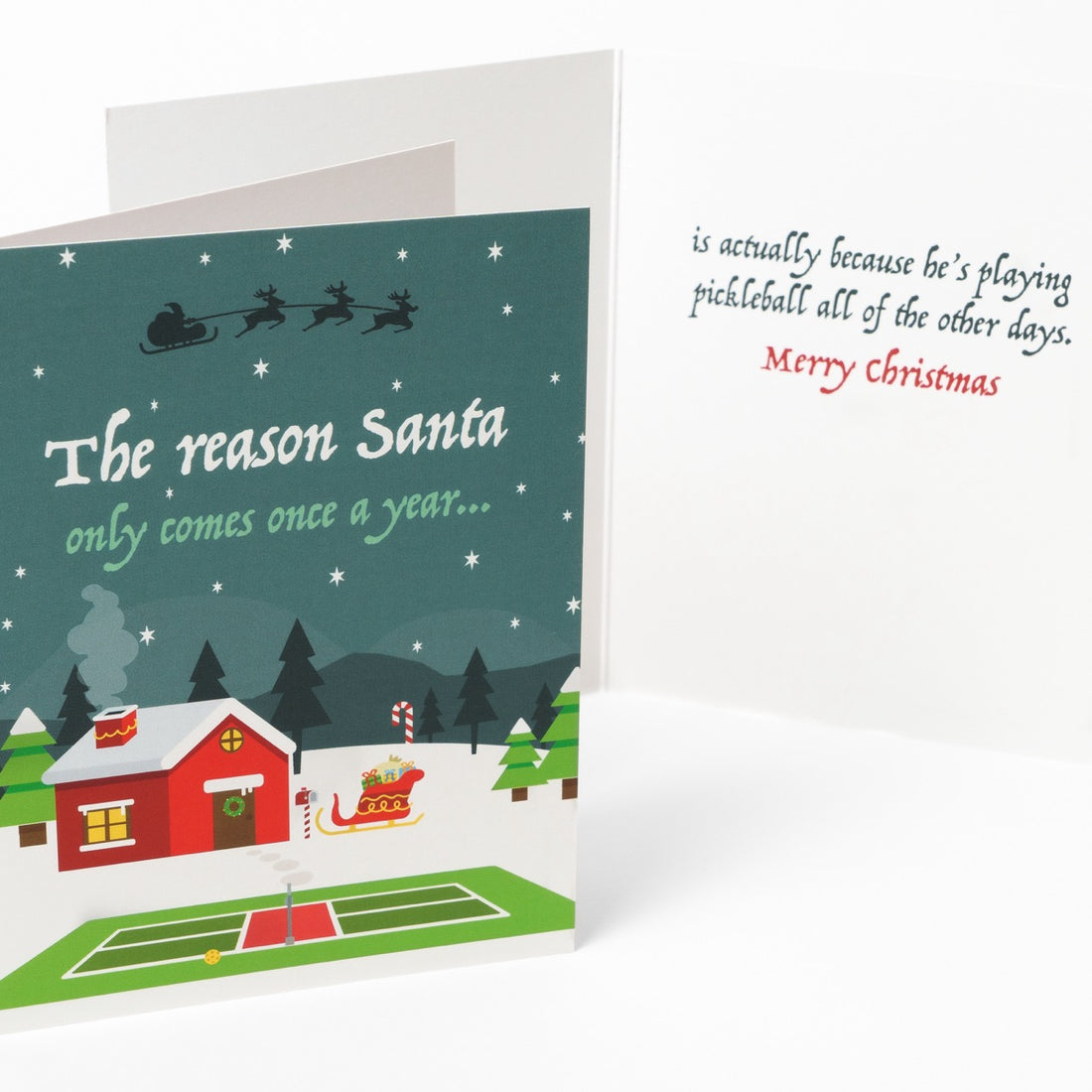 Front and inside message of a pickleball themed Christmas greeting card showing Santas home in the north pole with a pickleball court in the front with a message that says &quot;The reason Santa only comes once a year... is actually because he&