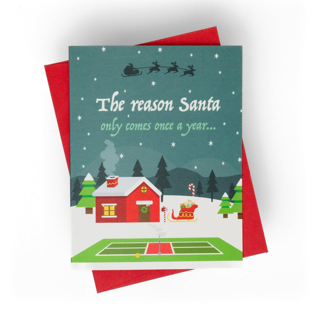 Pickleball themed Christmas greeting card showing Santas home in the north pole with a pickleball court in the front laying flat with a red envelope.