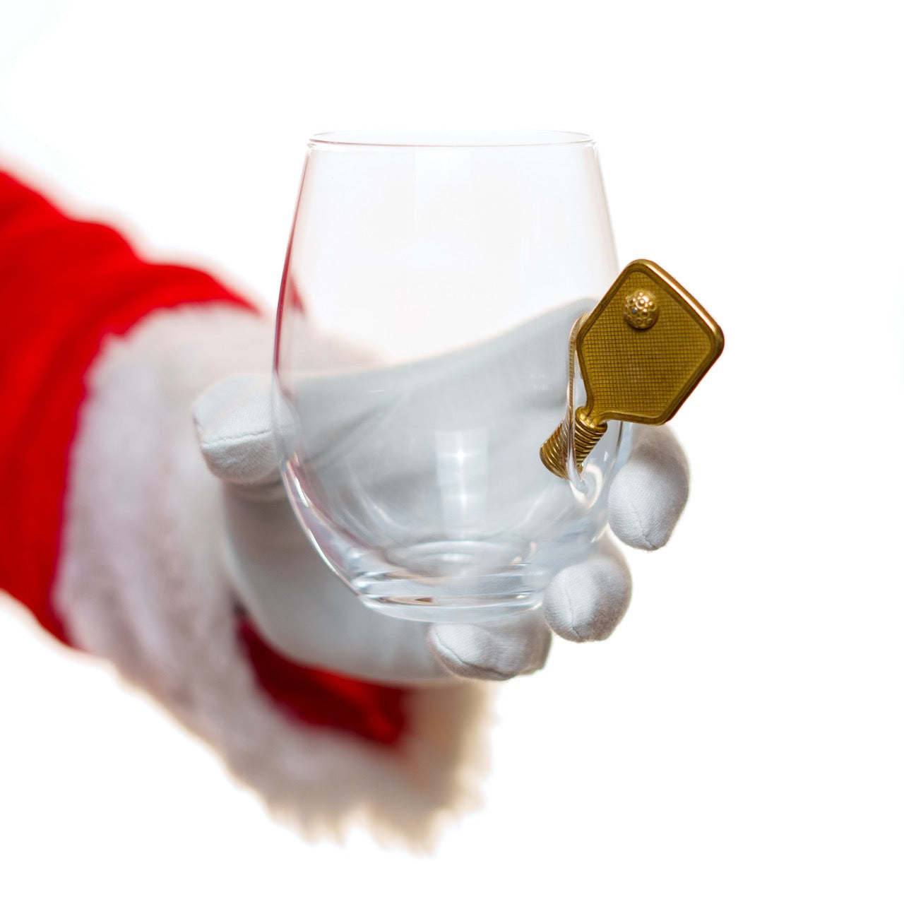 Santa holding a unique wine glass with a small metal pickleball paddle protruding from the side in front of a white studio backdrop