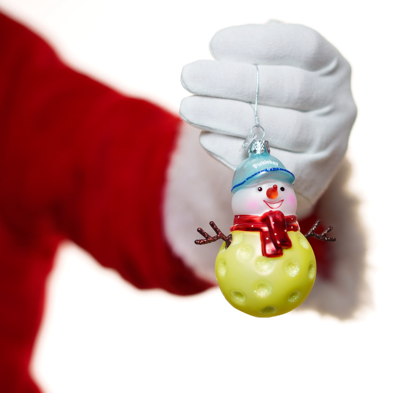 Santa holding a glass Christmas ornament of a pickleball snowman in front of a white studio backdrop