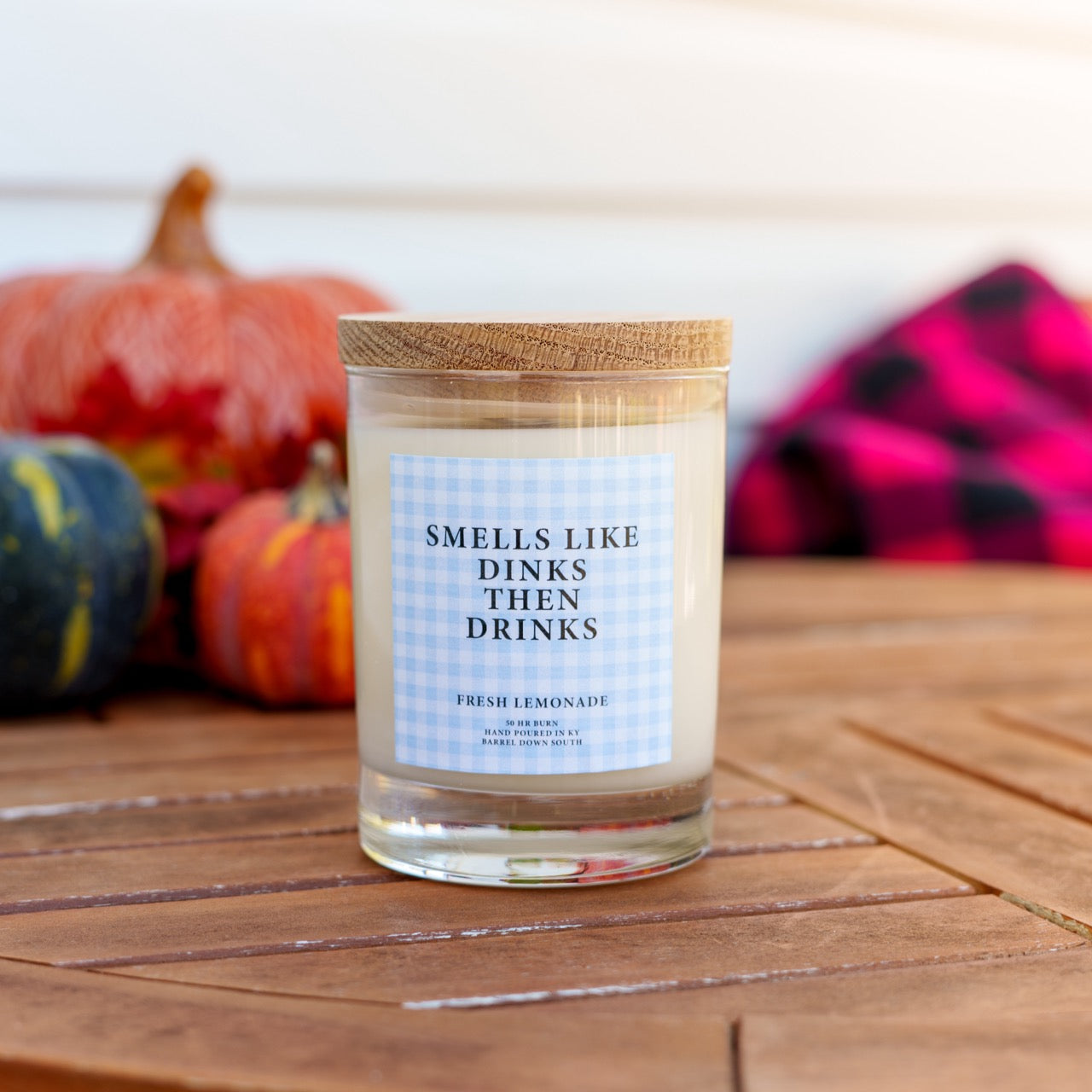 pickleball themed candle that says Smells Like Dink Then Drinks on a table in front of pumpkins and a blanket