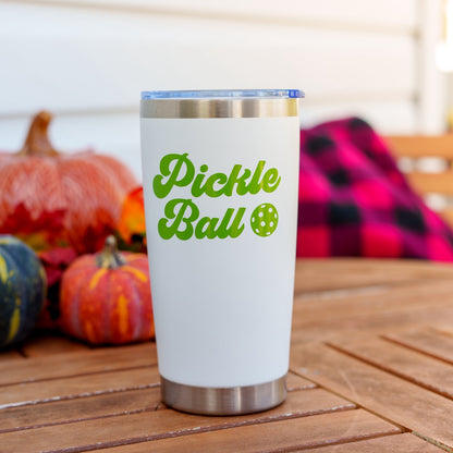 White and green tall tumbler that says Pickleball on a table in front of pumpkins and a blanket