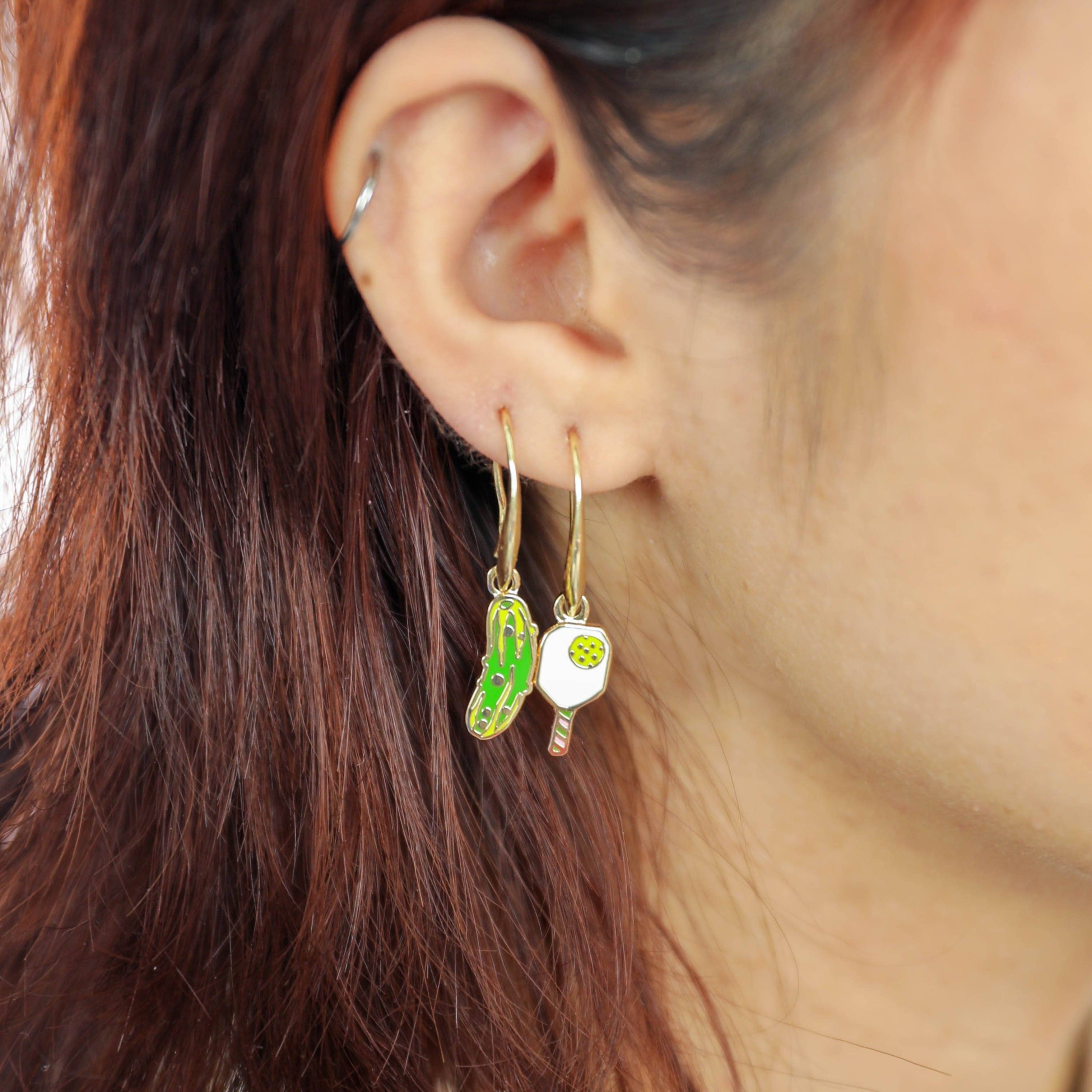 Women wearing earrings with a pickle on one and a pickleball paddle on the other