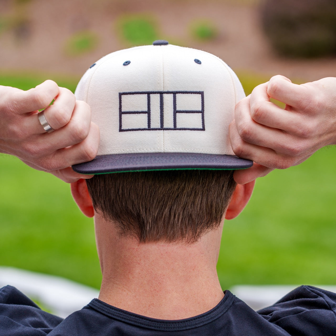 Man wearing a white and black flat brimmed hat with pickleball court lines embroidered on it