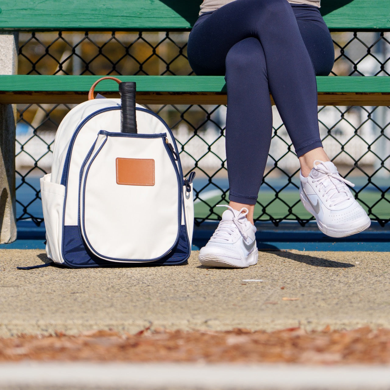 Woman sitting on a bench next to pickleball court with a stylish white pickleball paddle backpack.