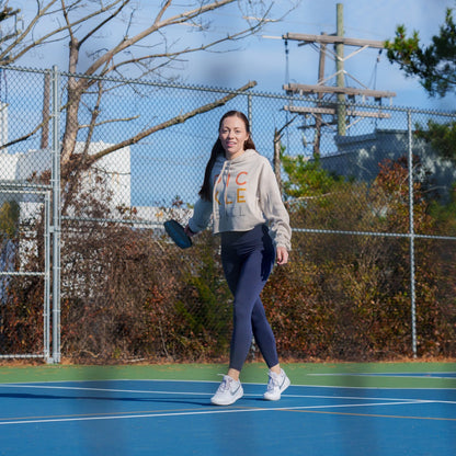 Woman on a pickleball court holding a pickleball paddle and wearing a cropped hoodie sweatshirt that says PICKLEBALL on it