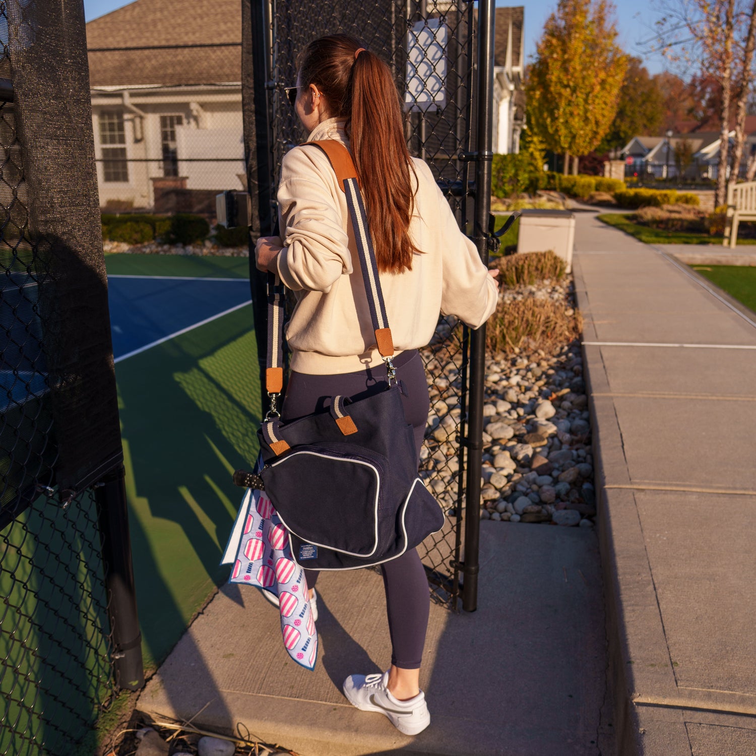 Woman walking onto a pickleball court with a bag and sports towel.