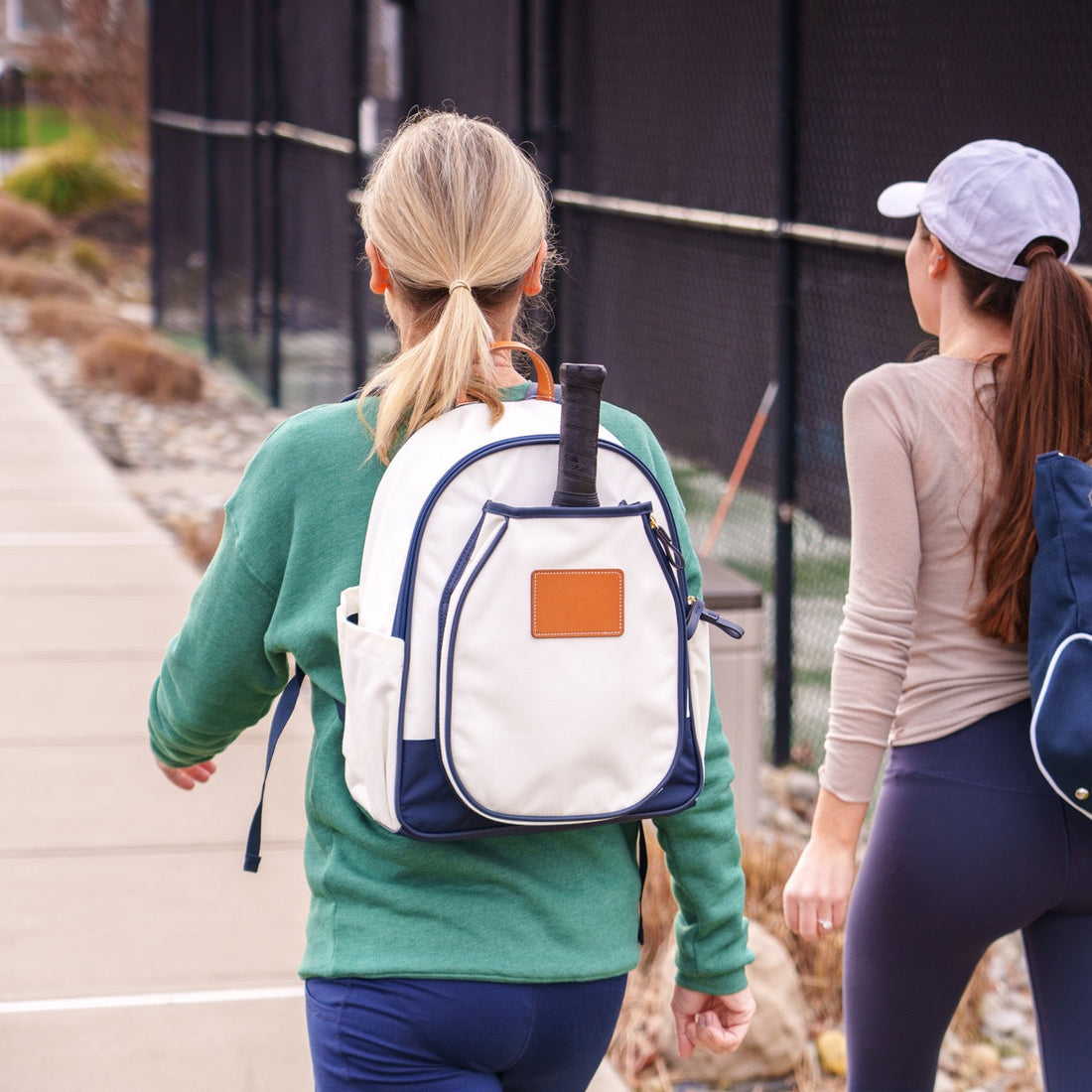 Two women walking to pickleball courts with one wearing a white pickleball backpack